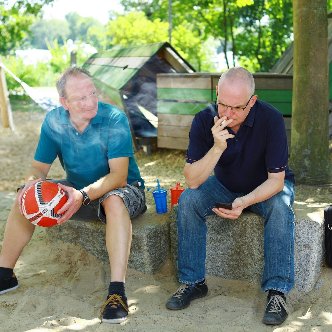 Zwei Männer sitzen im Freien auf einer Bank, einer hält einen Basketball in der Hand.